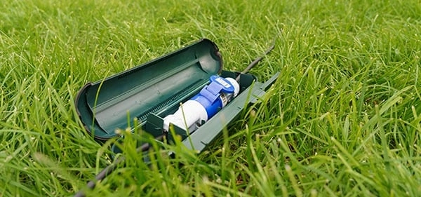 Groene waterdichte opbergbox met elektrische kabels en stekkers liggend in het gras, ideaal voor buitengebruik