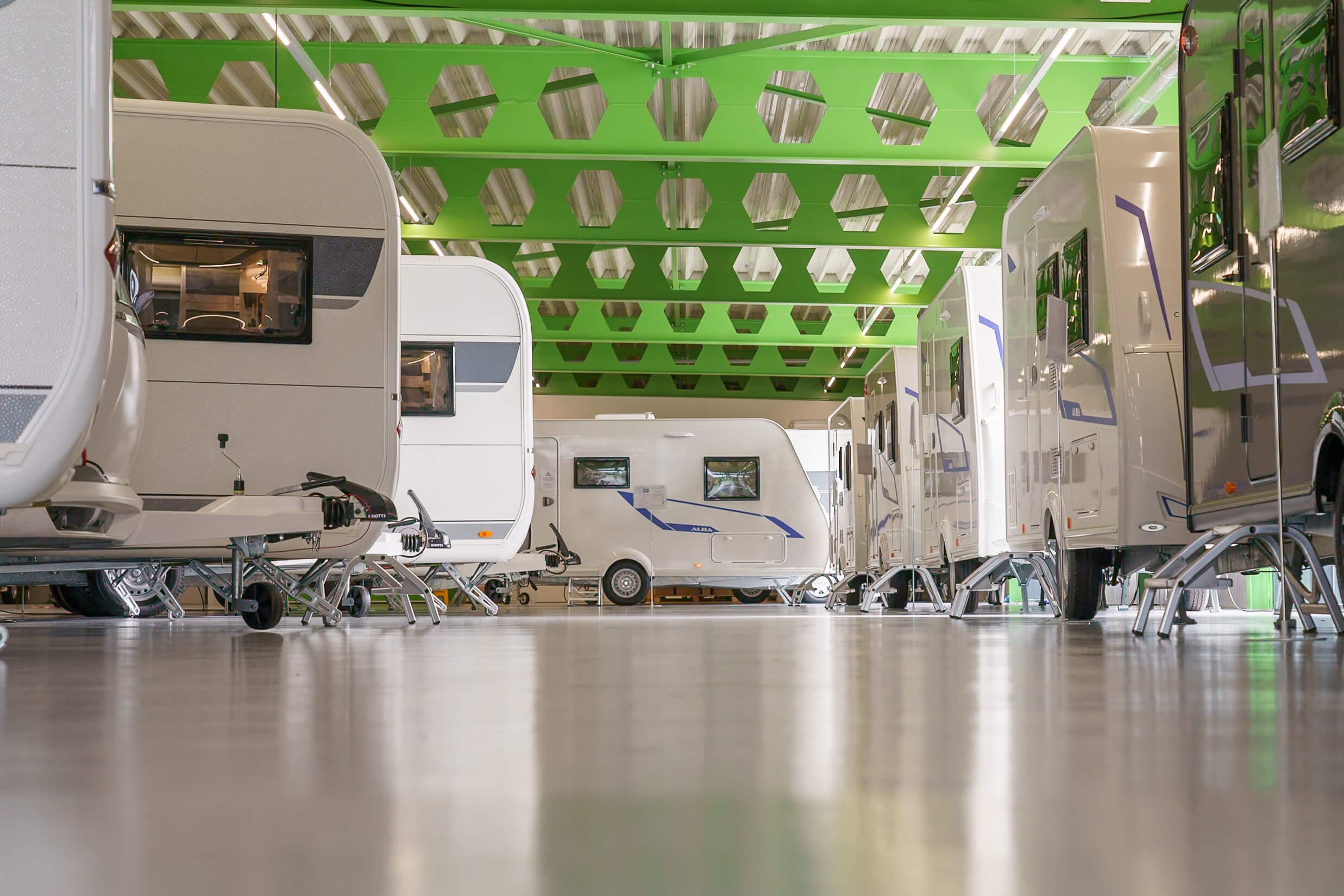 Moderne caravans in een ruime showroom met opvallend groen plafond en glanzende vloer, professioneel opgesteld voor verkoop of tentoonstelling.