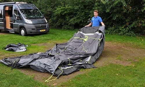 Opzetten van een grijze tent op kampeerplek Persoon zet een grijze tent op op een grasveld omringd door groen gebladerte