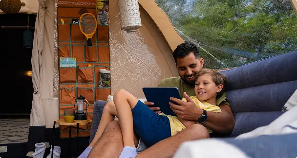 vader en zoon op opblaasbare bank Vader en zoon ontspannen samen op een opblaasbare bank in een luxe tent, kijkend naar een tablet terwijl ze genieten van hun glamping ervaring